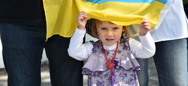 A girl looks out from under a Ukrainian national flag as relatives of new volunteer recruits of the Ukrainian army 'Donbass' battalion attend a military oath ceremony of the National Guard near the Novi Petrivtsi village not far from Kiev, on June 23, 2014. Some 600 new volunteer recruits of the battalion, mainly representatives of the eastern Donbass region of Ukraine, who followed combat training during three weeks will take part in the military operation against armed pro-Russian militants in the east of the country. Ukraine pressed German Chancellor Angela Merkel and other Western allies today to help end a pro-Russian uprising that has continued to rage in the industrial east despite Kiev's unilateral ceasefire. AFP PHOTO / SERGEI SUPINSKY (Photo credit should read SERGEI SUPINSKY/AFP/Getty Images)