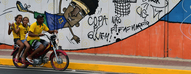 Tifosi del Brasile oltrepassano un murale realizzato per i Mondiali vicino allo stadio Castelào, a Fortaleza.
(AFP PHOTO / YURI CORTEZ)