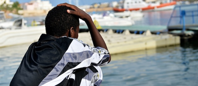 LAMPEDUSA, ITALY - OCTOBER 08: A surviving immigrant of the tragic shipwreck off the Italian coast looks on as Italian Navy and Coast Guard units take part of disembark operation of the bodies of the victims at Lampedusa harbour on October 8, 2013 in Lampedusa, Italy. The search for bodies continues off the coast of Southern Italy as the death toll of African migrants who drowned as they tried to reach the island of Lampedusa is expected to reach over 300 people. The tragedy has bought fresh questions over the thousands of asylum seekers that arrive into Europe by boat each year. (Photo by Tullio M. Puglia/Getty Images)