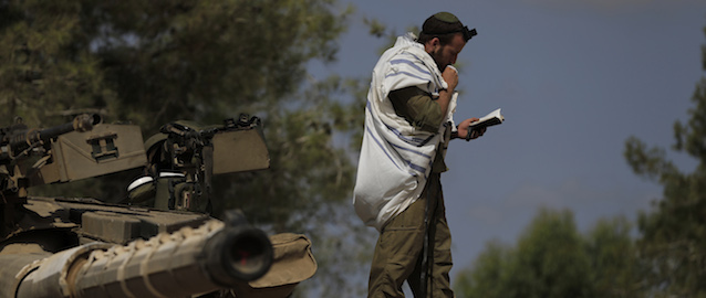 An Israeli soldier prays on the top of a tank near the Israel and Gaza border, Sunday, July 13, 2014. TIsrael briefly deployed ground troops inside the Gaza Strip for the first time early Sunday as its military warned northern Gaza residents to evacuate their homes, part of a widening offensive that has killed more than 160 Palestinians. (AP Photo/Tsafrir Abayov)
