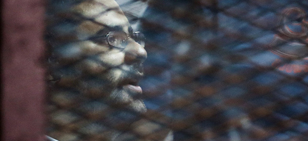 Prominent Egyptian activist Alaa Abdel Fattah stands behind bars as he is tried at the court in Cairo on August 6, 2014. Abdel Fattah and 24 other defendants are accused of illegally holding a protest and of assaulting a police officer during a demonstration outside the Shura council last November in objection to the military trials of civilians. AFP PHOTO/MOHAMED EL-SHAHED (Photo credit should read MOHAMED EL-SHAHED/AFP/Getty Images)
