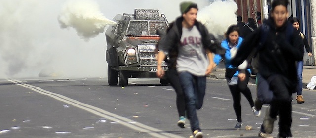 Protester run away from on oncoming tear gas truck, during a student protest march in Santiago, Chile, Thursday, Aug. 21, 2014. Tens of thousands of students protested in the third massive march of the year in Chile. The students are unhappy with the pace of education reform that President Michelle Bachelet has been moving forward. (AP Photo/Luis Hidalgo)