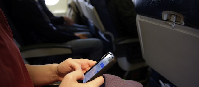 FILE - In this Oct. 31, 2013, file photo, a passenger checks her cell phone before a flight in Boston. The Federal Communications Commission might be ready to permit cellphone calls in flight. Old concerns about electronics being a danger to airplane navigation have been debunked. And carriers could make some extra cash charging passengers to call a loved one from 35,000 feet. But that extra money might not be worth the backlash from fliers who view overly-chatty neighbors as another inconvenience to go along with smaller seats and stuffed overhead bins. (AP Photo/Matt Slocum, File)