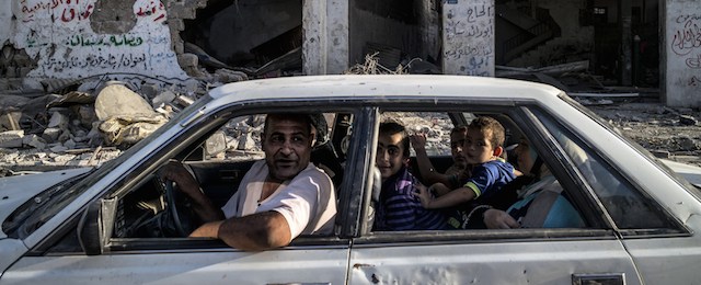 A Palestinian family drves past a destroyed building in the devastated neighbourhood of Shejaiya in Gaza City on August 6, 2014. Israeli Prime Minister Benjamin Netanyahu launched a vigorous defence of Israel's month-long conflict in Gaza as "justified" and "proportionate", blaming Hamas for the heavy Palestinian civilian death toll. AFP PHOTO/MARCO LONGARI (Photo credit should read MARCO LONGARI/AFP/Getty Images)