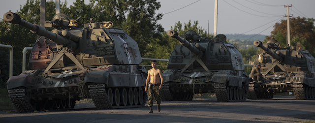 In this photo taken Thursday, Aug. 14, 2014, a Ukrainian soldier walks past self-propelled guns as an army column of military vehicles prepares to roll to a frontline near Illovaisk, Donetsk region, eastern Ukraine. Ukrainian forces have stepped up efforts to dislodge the separatists from their last strongholds in Donetsk and Luhansk and there was more heavy shelling overnight. (AP Photo/Evgeniy Maloletka)