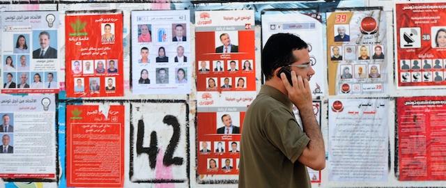 A Tunisian speaks on the phone as he walks past election posters put up on a street ahead of the parliamentary election in the Tunis suburb of Ariana on October 21, 2014. Tunisians vote on October 26, 2014 to elect their first parliament since the country's 2011 revolution, in a rare glimmer of hope for a region torn apart by post-Arab Spring violence and repression. AFP PHOTO / FETHI BELAID (Photo credit should read FETHI BELAID/AFP/Getty Images)