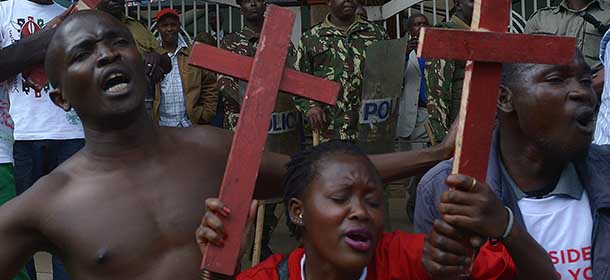 Kenyan police forces stand guard as protesters shout slogans while holding wooden crosses representing those killed in a string of attacks during a demonstration in Nairobi to demand greater security on November 25, 2014 as thousands of Kenyan civil servants were urged to leave troubled regions hit by a wave of insurgent attacks. The warnings by six unions to members to leave the restive northeast, as well as the protests in Nairobi, follow a weekend attack which saw 28 non-Muslims executed on a bus. Kenya has suffered a series of attacks since invading Somalia in 2011 to strike the Shebab, later joining an African Union force battling the Islamists. AFP PHOTO/TONY KARUMBA (Photo credit should read TONY KARUMBA/AFP/Getty Images)
