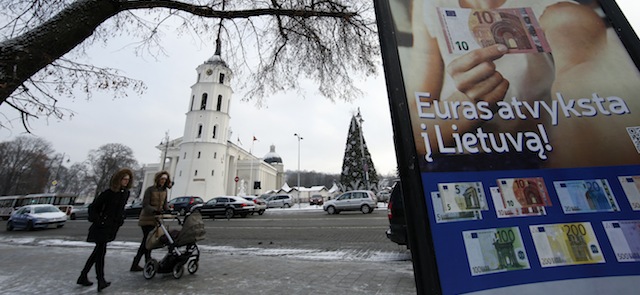 People walk by a poster reading "The euro is coming to Lithuania" in Vilnius, Lithuania, Monday, Dec. 29, 2014. Political leaders are hoping that joining the euro on Jan. 1 will help Lithuania distance itself further from Russian influence, reduce government borrowing costs and make. (AP Photo/Mindaugas Kulbis)