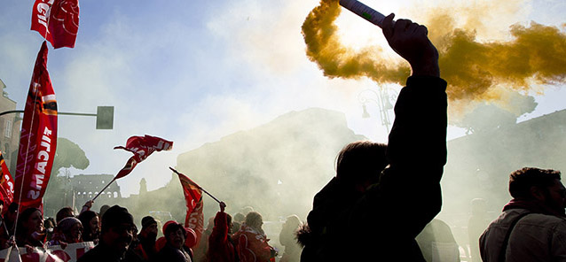 A demonstrator holds a flare during a protest in Rome, Friday, Dec. 12, 2014. Thousands of union workers and students staging a general strike marched Friday through more than 50 Italian cities to protest government reforms that they say erode workers' rights. The general strike, shutting down basic services across Italy, is the first ever by two of Italy's largest union confederations against a center-left government, which have traditionally cozied up to unions. Premier Matteo Renzi said the right to strike must be protected, but insisted his tougher line is necessary to return the economy to growth and create jobs. (AP Photo/Alessandra Tarantino)
