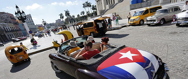 Tourists take a ride in a classic American convertible car with the Cuban national flag painted on the trunk, in Havana, Cuba, Thursday, Dec. 18, 2014. After a half-century of Cold War acrimony, the United States and Cuba abruptly moved on Wednesday to restore diplomatic relations, a historic shift that could revitalize the flow of money and people across the narrow waters that separate the two nations. (AP Photo/Desmond Boylan)