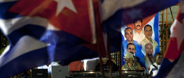 Cuban flags fly near to a poster of photographs of five Cuban intelligence agents who are imprisoned in U.S. during a concert marking the 14th anniversary of their arrests in Florida in 1998, in Havana, Cuba, Wednesday, Sept 12, 2012. (AP Photo/Ramon Espinosa)