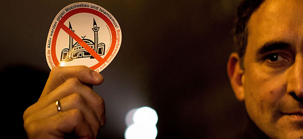 BERLIN, GERMANY - JANUARY 05: A supporter of the Pegida movement holds a sticker with a crossed mosque symbol while supporters gather for a march in their first Berlin demonstration, which they have dubbed "Baergida," on January 5, 2015 in Berlin, Germany. Pegida is an acronym for 'Patriotische Europaeer Gegen die Islamisierung des Abendlandes,' which translates to 'Patriotic Europeans Against the Islamification of the West,' and has quickly gained a spreading mass appeal by demanding a more restrictive policy on Germany's acceptance of foreign refugees and asylum seekers. While Pegida disavows xenophobia in its public statements, critics charge that the movement is becoming a conduit for right-wing activists. The first Pegida march took place in Dresden in October and has since attracted thousands of participants to its weekly gatherings that have also begun spreading to other cities in Germany. Germany is accepting a record number of refugees this year, especially from war-torn Syria, and the country has also witnessed the rise of Salafist movements in numerous immigrant-heavy German cities. Both phenomena have promoted Pegida's rise and appeal. (Photo by Carsten Koall/Getty Images)