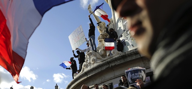Demonstrators wave flags on the monument at the center of Republique Square before the demonstration, in Paris, France, Sunday, Jan. 11, 2015. A rally of defiance and sorrow, protected by an unparalleled level of security, on Sunday will honor the 17 victims of three days of bloodshed in Paris that left France on alert for more violence. (AP Photo/Laurent Cipriani)