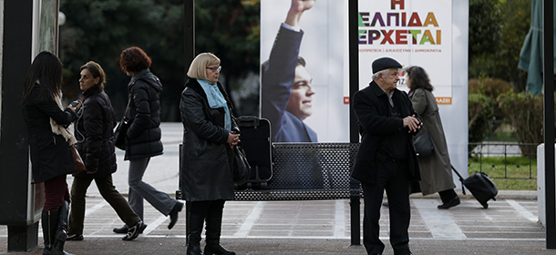 Commuters wait at a bus stop as pedestrians pass a banner reads in Greek ''Hope is on the way'' with the photograph of the opposition leader Alexis Tsipras at the election kiosk of the anti-bailout Syriza party, in central Athens, on Wednesday, Jan. 14, 2015. Samaras' New Democracy party is facing elections on Jan. 25 and trailing in opinion polls to the leftwing Syriza party, which is demanding that at least half of the Greece's 240 billion euro ($283 billion) bailout loans be forgiven. (AP Photo/Thanassis Stavrakis)