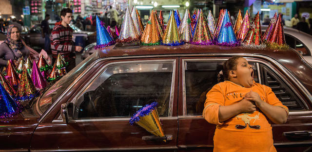 Una ragazzina egiziana sbadiglia appoggiata a una macchina usata come bancarella per vendere cappellini da festa, al Cairo. (AP Photo/Eman Helal)