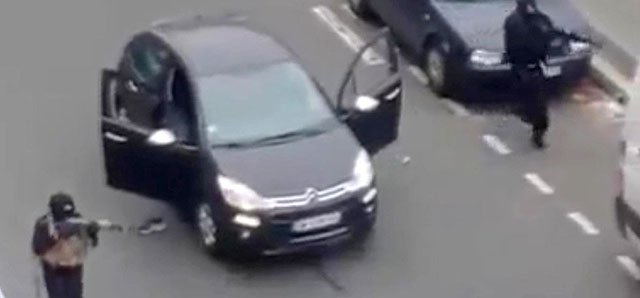 Masked gunman fire their weapons outside the French satirical newspaper Charlie Hebdo's office, in Paris, Wednesday, Jan. 7, 2015. Paris residents captured chilling video images of two masked gunmen shooting a police officer after an attack at a French satirical newspaper. In the video, the gunmen armed with assault rifles are seen running up to an injured police officer, who lies squirming on the ground. The police officer raises his hands up before one of the assailants shoots him in the head at a close range. (AP Photo) NO SALES