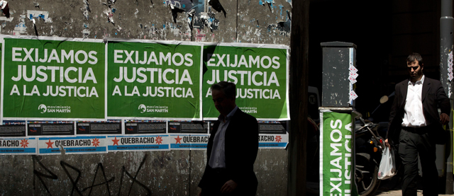 Men walk pass posters that read in Spanish "Demand justice to justice", in reference to march organized by federal prosecutors demanding justice after the death of special prosecutor Alberto Nisman almost a month ago, in Buenos Aires, Argentina, Friday, Feb. 13, 2015. Nisman accused President Cristina Fernandez, Foreign Minister Hector Timerman and others in her administration of brokering the cover-up in the bombing of a Jewish community center in exchange for favorable deals on oil and other goods from Iran. Fernandez and Timerman have strongly denied the accusations, and Iran has repeatedly denied involvement in the bombing, which killed 85 people. (AP Photo/Rodrigo Abd)