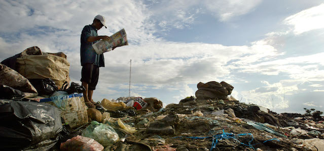 PHNOM PENH, CAMBODIA - JULY 26: A Cambodian man reads a newspaper while going through the garbage at a garbage dump looking for things to recycle in order to survive July 26, 2003 in Phnom Penh, Cambodia. Rampant corruption in this impoverished country has lead to extreme poverty with many Cambodians living below the poverty line. Roughly six million Cambodians will go to the polls tomorrow hoping for their lives to improve with the upcoming national elections, the third democratic election in ten years. (Photo by Paula Bronstein/Getty Images)
