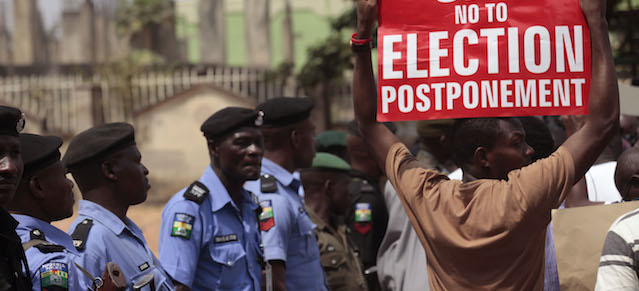 A protestor holds a banner as Nigerian security forces look on, during a protest in Abuja, Nigeria, Saturday, Feb. 7, 2015, against the possible postponement of the Nigerian elections. Civil rights groups staged a small protest Saturday against any proposed postponement. (AP Photo/Lekan Oyekanmi)