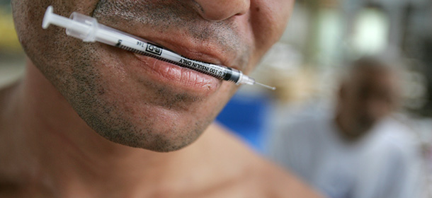 An addict keeps a syringe in his mouth as he heats heroin powder before injecting himself, inside one of the many so-called "shooting galleries," where addicts gather, in downtown San Juan, Puerto Rico, Monday, Oct. 3, 2005. As a U.S. Territory, Puerto Rico is a convenient transit point for drug smugglers en route to the United States from South America, and addiction rates on the Island are epidemic, according to health professionals. (AP Photo/Brennan Linsley)