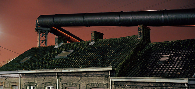 The gas supply tubes run along the houses built near the steel factories of Charleroi. Before the electric upgrade of the blast furnace these tubes used to provide the energy necessary to this operation. The factory and furnace infringe and loom over the lives of the inhabitants.