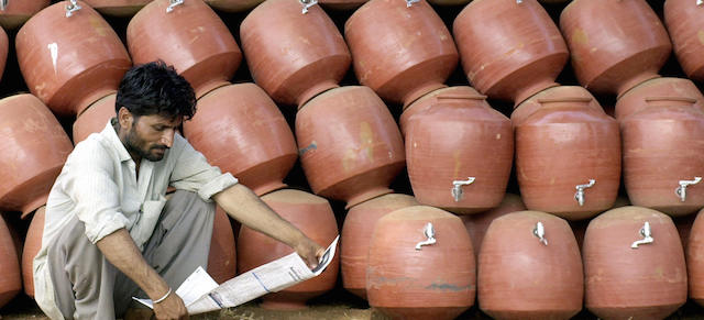 MADRAS, INDIA: An unidentified Indian vendor reads a newspaper at his road side water-pot stand in Madras, 18 February 2004. The vendor brought his range of specially made ceramic water-pots fitted with taps in the western Indian state of Rajasthan, and he claims that they are the most cost-effective, eco-friendly natural water cooling option available on the Indian market. AFP PHOTO/Dibyangshu SARKAR (Photo credit should read DIBYANGSHU SARKAR/AFP/Getty Images)