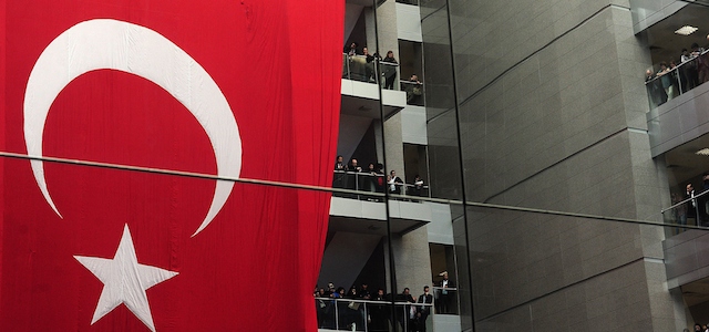 People stand on April 1, 2015 near a large Turkish flag during a funeral ceremony for senior Istanbul prosecutor Mehmet Selim Kiraz, killed the day before after being held at his offices by leftist militants in a hostage drama, inside the courthouse where the hostage taking took place in Istanbul. Kiraz had been investigating the politically-sensitive case of a teenager who died of injuries inflicted by police during anti-government protests in 2013. Turkish authorities on April 1 rounded up over 30 suspected members of the radical leftist group behind a bloody hostage standoff that left a top Istanbul prosecutor dead and shocked the country. AFP PHOTO / OZAN KOSE (Photo credit should read OZAN KOSE/AFP/Getty Images)