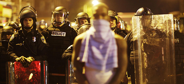 A man stands in front of a line of police officers in riot gear as part of a community effort to disperse the crowd ahead of a 10 p.m. curfew in the wake of Monday's riots following the funeral for Freddie Gray, Tuesday, April 28, 2015, in Baltimore. (AP Photo/David Goldman)