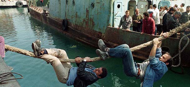 Two Albanian men climb down a rope to get aboard a boat leaving for Italy in the Albanian port of Durre Friday, March 14, 1997. Civil unrest has spread throughout Albania after an armed rebellion in the south of the country caused most police and army to abandon their posts to mobs enraged by losing money in failed investment schemes. (AP Photo/Santiago Lyon)