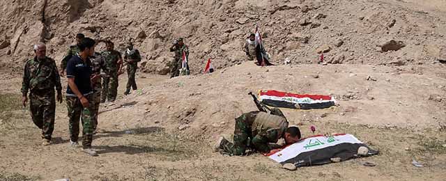 Iraqi security forces and allied Shiite militiamen pray at a cemetery at Camp Speicher for soldiers killed near Salah al-Din palace, one of Saddam Hussein's palaces in Tikrit, 80 miles (130 kilometers) north of Baghdad, Iraq, Friday, April 3, 2015. (AP Photo/Khalid Mohammed)