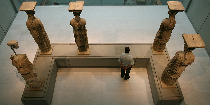 A visitor to the new Acropolis museum stands behind the Caryatids, female figures used instead of pillars, in Athens on Sunday, June 21, 2009. The empty space in front of the visitor denotes the absence of a Caryatid now on display at the British Museum in London. The Acropolis Museum opened its gates today to the first visitors who came to see the more than 4,000 exhibits on display, including those parts of Parthenon's marble frieze not held by the British Museum. (AP Photo/Thanassis Stavrakis)