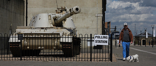A man walks his dog past a 2S3 M-1973 Akatsiya 152-mm self-propelled gun howitzer tank stands outside the Greenwich Heritage Centre, set up as a polling station in London on May 7, 2015, as Britain holds a general election. Polls opened today in Britain's closest general election for decades with voters set to decide between the Conservatives of Prime Minister David Cameron, Ed Miliband's Labour and a host of smaller parties. AFP PHOTO / DANIEL SORABJI (Photo credit should read DANIEL SORABJI/AFP/Getty Images)