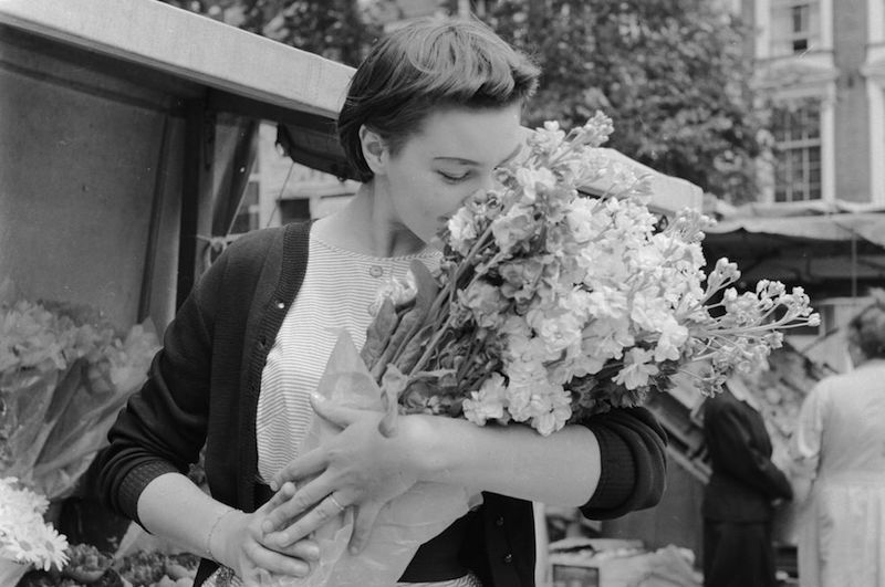 Circa 1955: A woman smelling a bouquet of Springtime flowers in a street in Holland. (Photo by Evans/Three Lions/Getty Images)