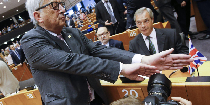 Il presidente della Commissione europea, Jean-Claude Juncker, scherza con un fotografo che sta inquadrando Nigel Farage dello Ukip nell'aula del Parlamento europeo (EPA/OLIVIER HOSLET)