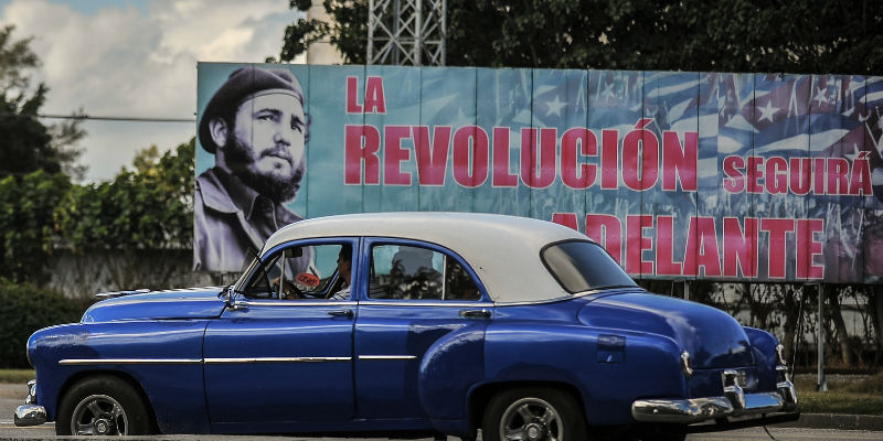 Un'auto a l'Avana passa vicino a un cartello con un'immagine di Fidel Castro e la scritta "La rivoluzione proseguirà", il 27 novembre 2016 (YAMIL LAGE/AFP/Getty Images)