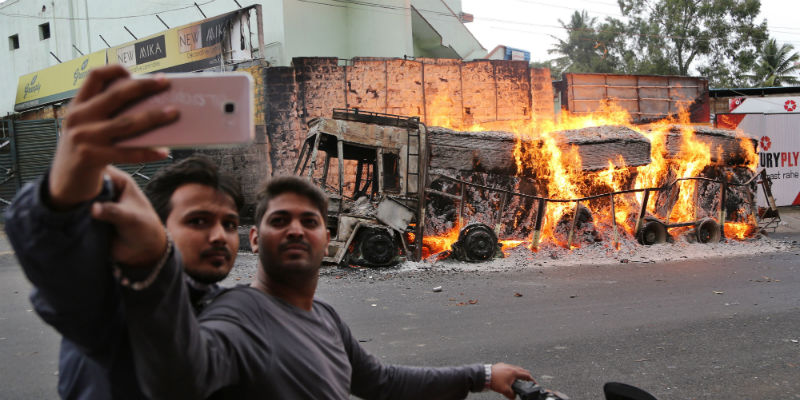 Due uomini si fanno un selfie davanti a un camion dato alle fiamme a Bangalore, nello stato indiano del Karnataka, il 12 settembre 2016 (AP Photo/Aijaz Rahi)