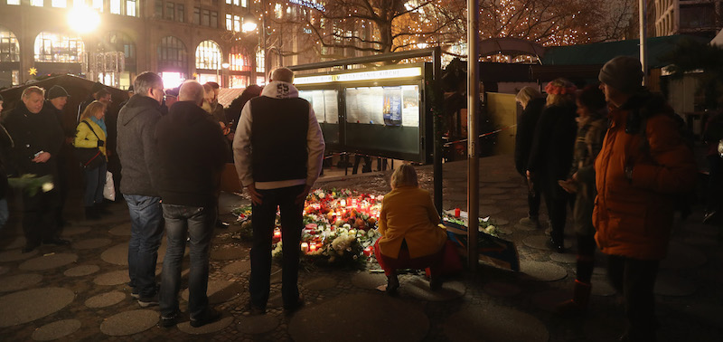 Un gruppo di persone davanti ai fiori e le candele portate al mercato dell'attentato di lunedì sera a Berlino. (Sean Gallup/Getty Images)