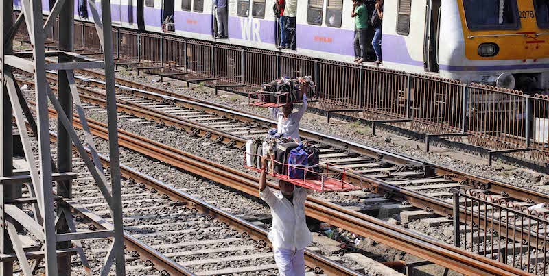 Un dabbawala cammina lungo i binari del treno per andare a consegnare le gavette con il pranzo ai suoi clienti (AP Photo/Rajesh Kumar Singh)