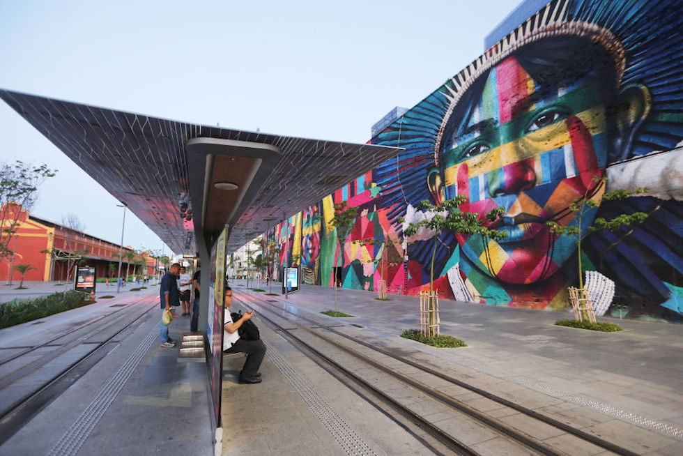 Un gruppo di persone aspetta il tram vicino a un murale dell'artista brasiliano Eduardo Kobra, disegnato in occasione delle Olimpiadi del 2016 a Rio de Janeiro (Mario Tama/Getty Images)