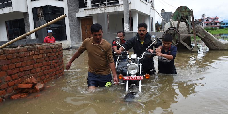 Un gruppo di nepalesi spinge una motocicletta in una strada allagata a Patan, alla periferia di Katmandu, il 13 agosto 2017 (PRAKASH MATHEMA/AFP/Getty Images)