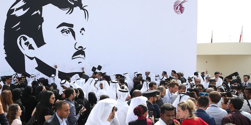 Dipendenti della Qatar Airways di fronte a un ritratto dell'emiro del Qatar, Tamim bin Hamad Al Thani, a Doha (STRINGER/AFP/Getty Images)
