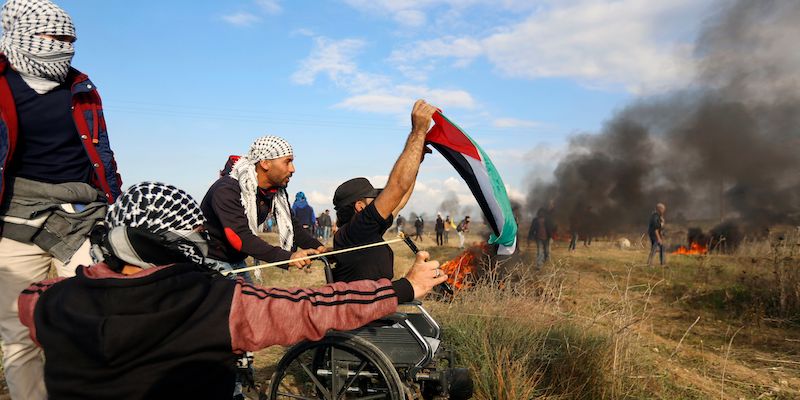 Un gruppo di palestinesi durante gli scontri con i soldati israeliani lungo il confine della Striscia di Gaza, il 15 dicembre 2017; l'uomo sulla sedia a rotelle che sventola la bandiera palestinese è uno di quelli morti nel corso della giornata (MOHAMMED ABED/AFP/Getty Images)