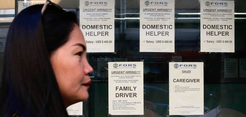 Una donna passa davanti agli annunci di lavoro per domestiche a Manila. (AP Photo/Aaron Favila)