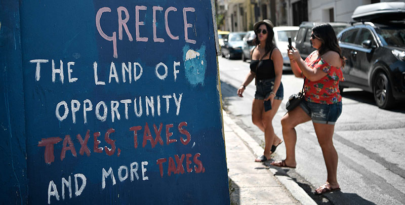 Delle turiste accanto a una scritta di protesta contro l'austerità, Atene, 18 agosto 2018 (LOUISA GOULIAMAKI/AFP/Getty Images)