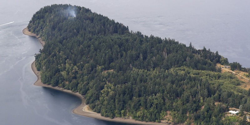 L'isola di Ketron, nello stretto di Pudget, l'11 agosto 2018: il punto in cui il 10 agosto è precipitato l'aereo di Horizon Air rubato da un dipendente della compagnia si riconosce per il fumo (AP Photo/Ted S. Warren)