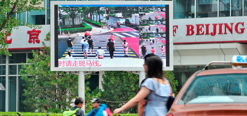 Un grosso schermo che mostra il sistema di identificazione per riconoscimento facciale di chi commette delle infrazioni attraversando la strada, a un incrocio di Pechino. (Imaginechina via AP Images)