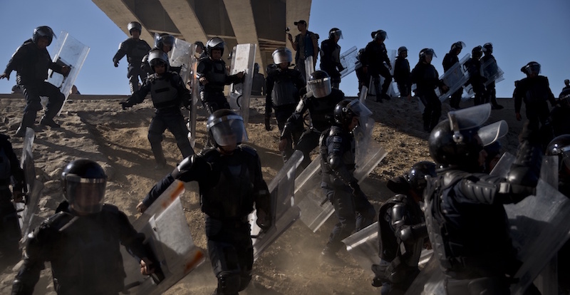 Agenti della polizia messicana inseguono i migranti lungo la scarpata del letto di un fiume per impedire loro di avvicinarsi al confine tra Messico e Stati Uniti (AP Photo/Ramon Espinosa)