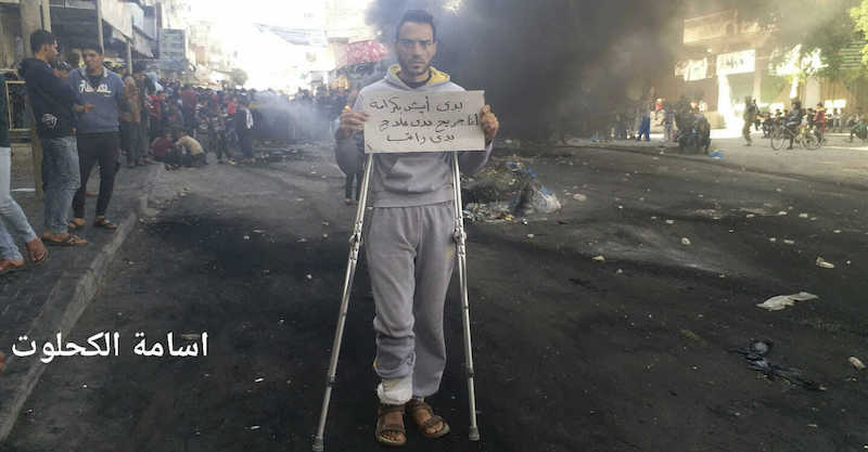 Un uomo con un cartello in mano che dice: «Voglio vivere con dignità; sono ferito e ho bisogno di cure mediche e di uno stipendio», durante una protesta nella Striscia di Gaza il 15 marzo 2019 (Osama al-Kahlout via AP)