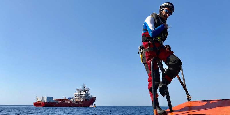 Un membro dell'ong SOS Mediterranee e sullo sfondo la nave Ocean Viking, il 5 agosto 2019 (La Presse / Anne CHAON / AFP)