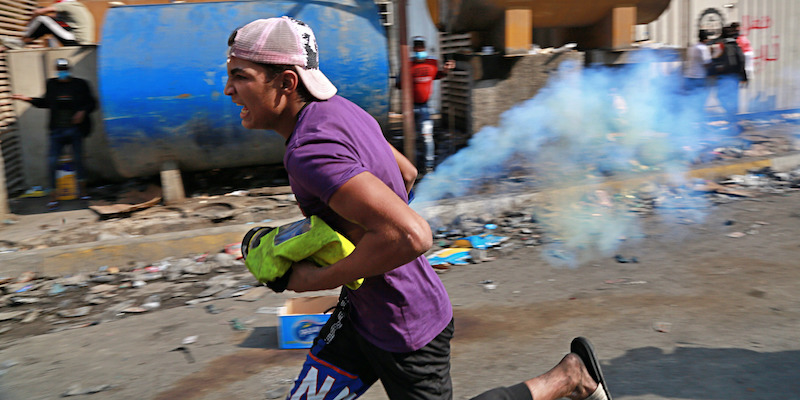 Un manifestante iracheno che si prepara a rilanciare una bomboletta di gas lacrimogeno lanciata dalla polizia a Baghdad, il 13 novembre 2019 (AP Photo/Khalid Mohammed)